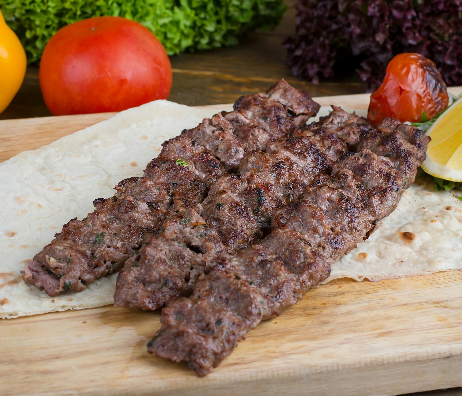 Kebab z szarpaną wołowiną i prażoną cebulką dla mięsożerców Kebab z wołowiną, warzywami i pieczywem podany na drewnianej desce