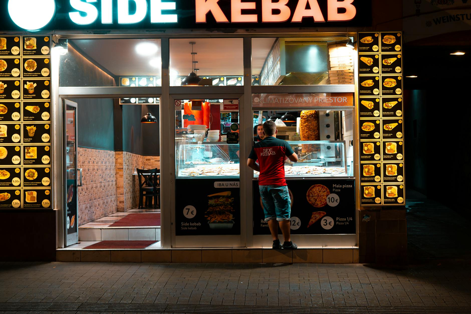 Nocna fasada baru z kebabem z podświetlonym menu i klientem przed wejściem