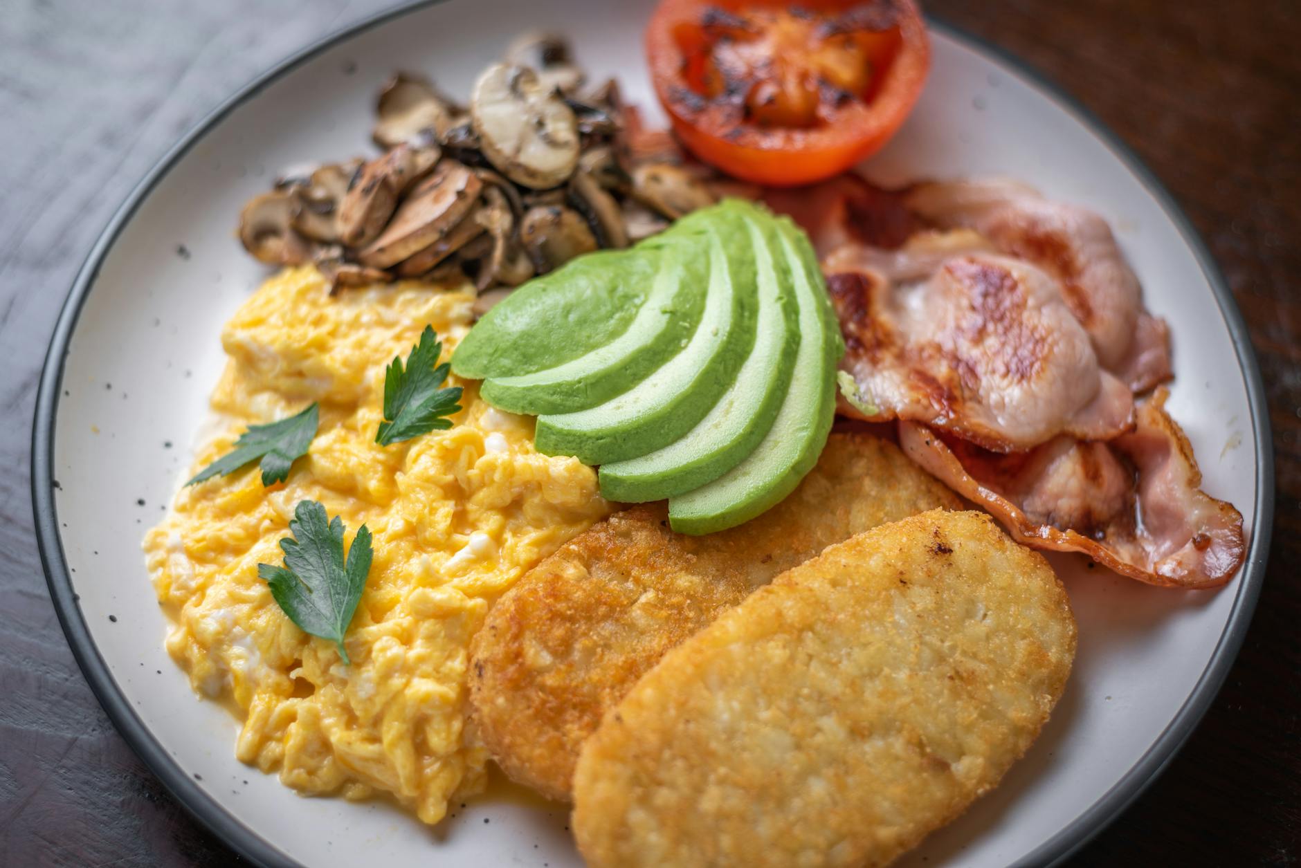 Śniadaniowy talerz z jajecznicą, awokado, boczkiem i ziemniaczanymi plackami